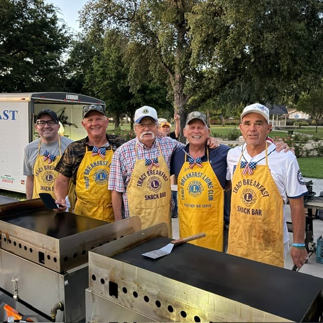 Club volunteers in yellow aprons behind outdoor griddles.